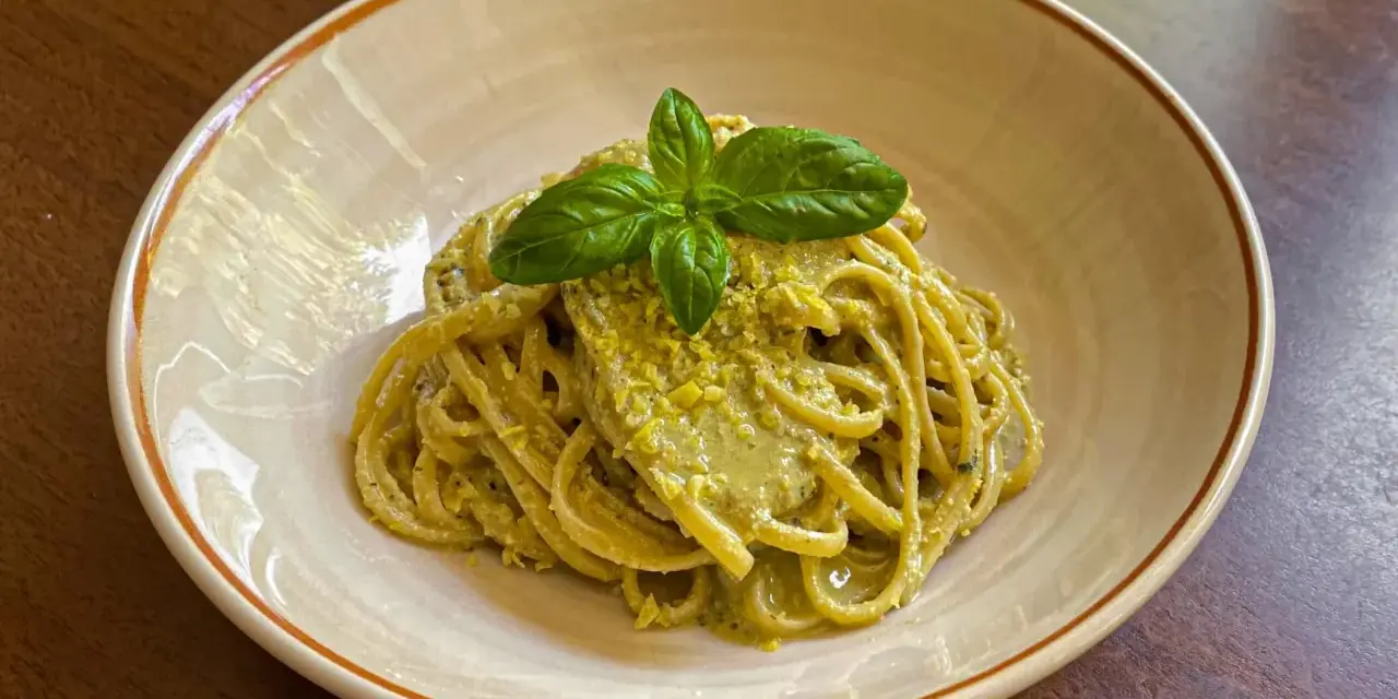 Spaghetti conditi con un cremoso pesto di limone, guarniti con basilico fresco. Una deliziosa ricetta per un primo piatto estivo.