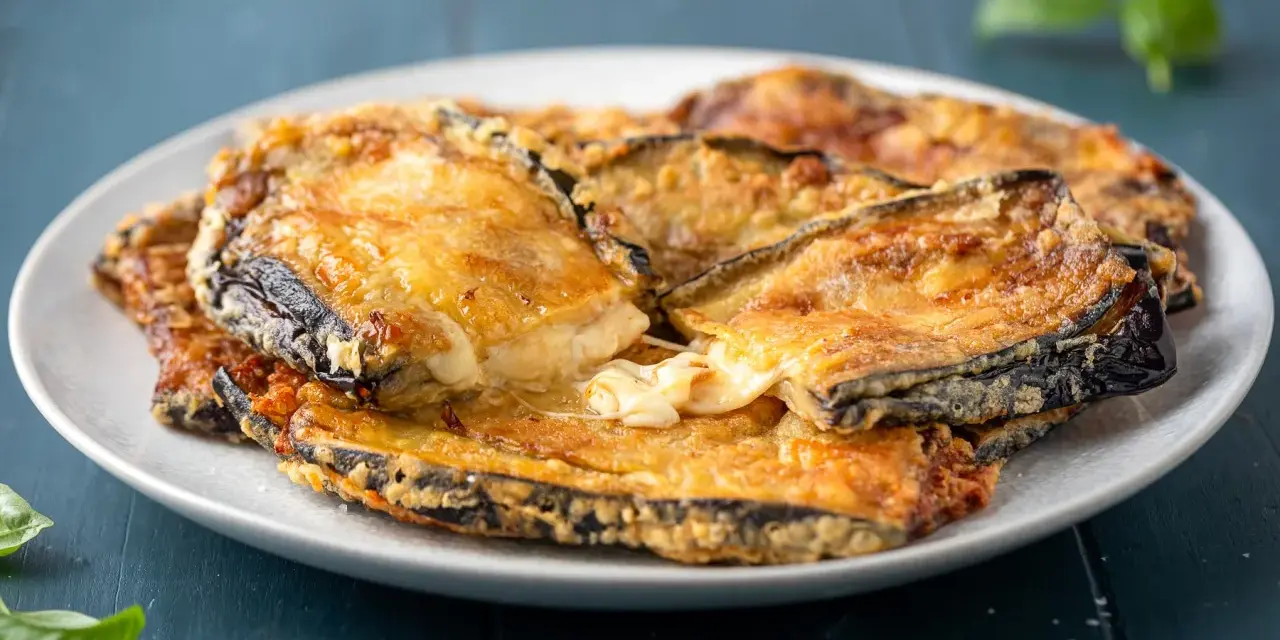 Melanzane contorno dorate e filanti, un piatto invitante con formaggio fuso e basilico fresco.