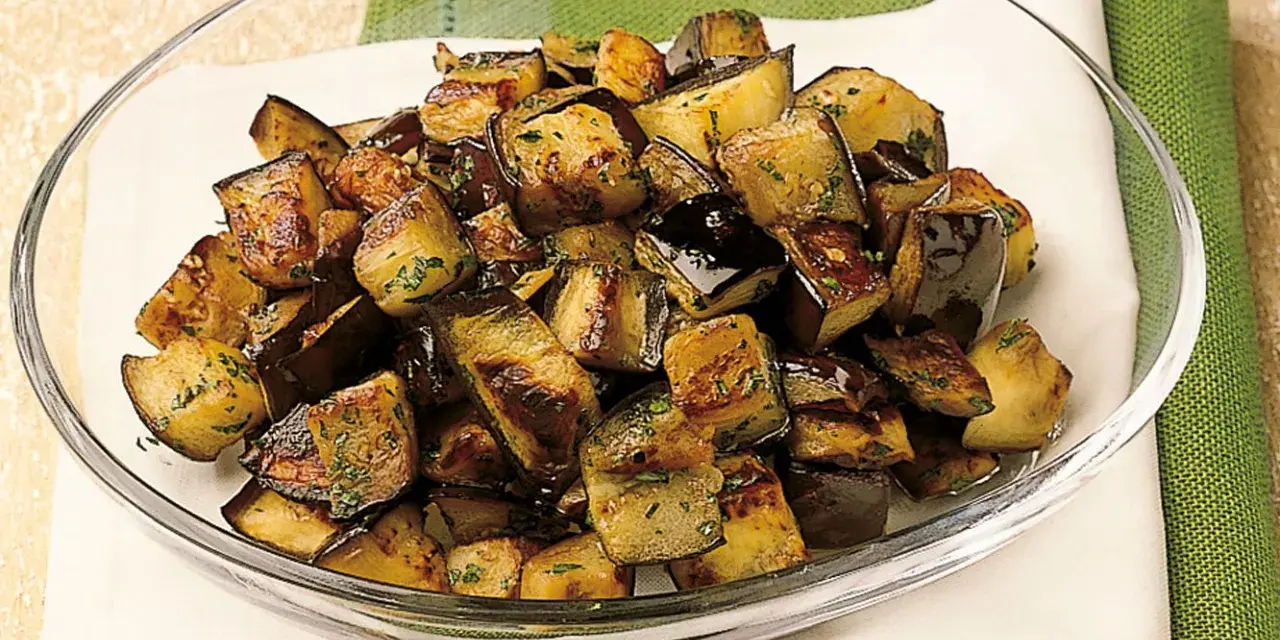 Melanzane a funghetto ricetta della nonna: cubetti dorati e saporiti, conditi con erbe aromatiche, in una ciotola di vetro.
