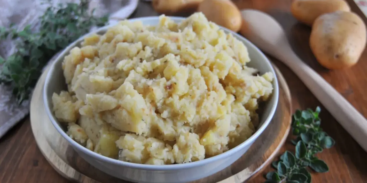 Un saporito piatto di patate in tecia, cotte con erbe aromatiche e spezie, servite in una ciotola su un tagliere di legno.
