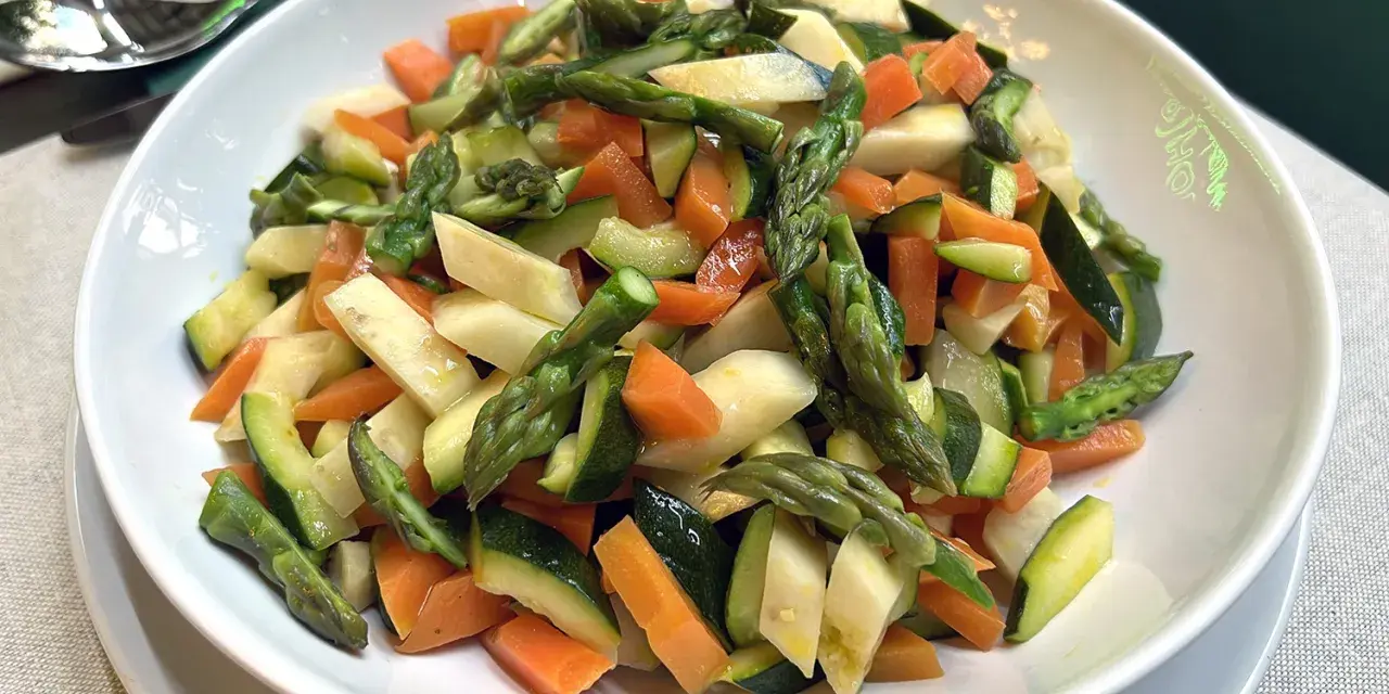 Un piatto invitante di verdure in padella: asparagi, carote e zucchine tagliate a pezzetti, condite con un filo d'olio.