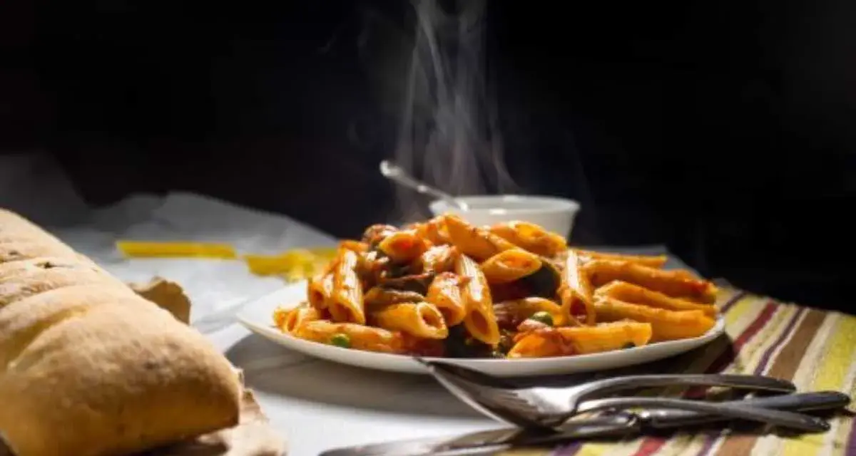 Piatto fumante di penne alla vodka, con pane croccante e posate pronte per gustare questo classico italiano.