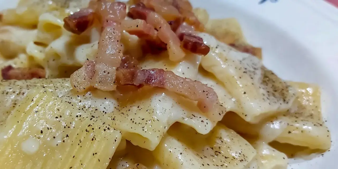 Un piatto di pasta alla gricia fumante, con guanciale croccante e abbondante pepe nero.