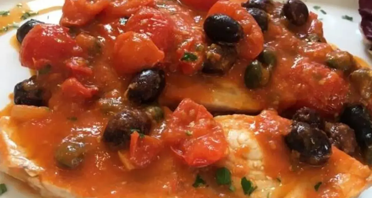 Delizioso pesce spada al forno con pomodorini, olive nere e capperi, un piatto saporito e colorato.