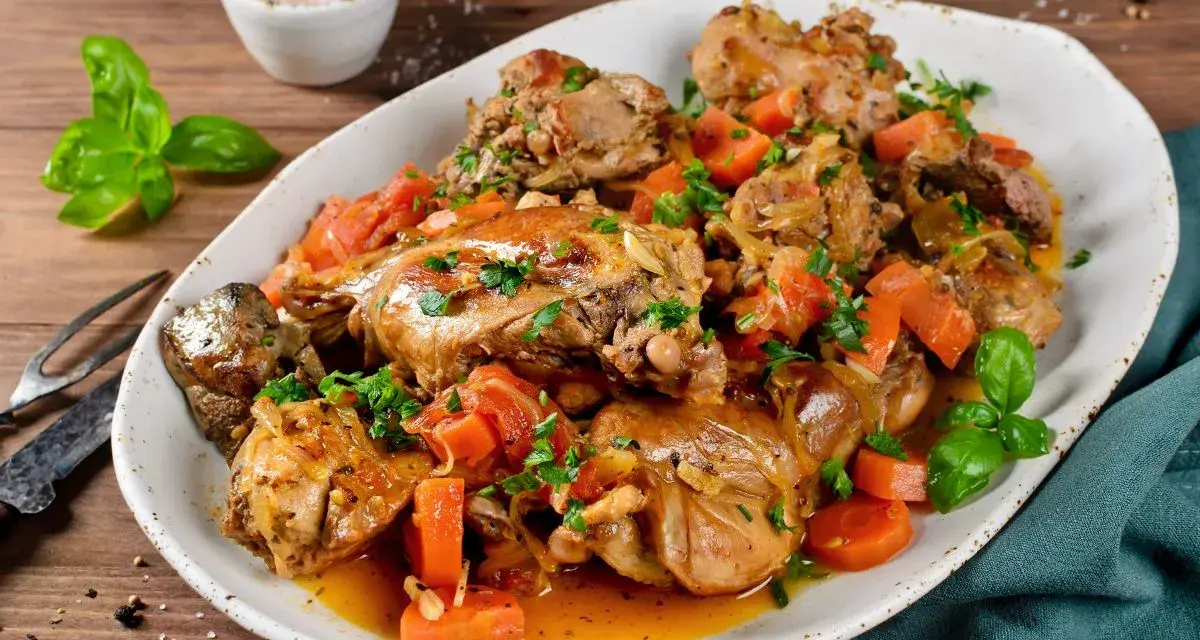 Un saporito coniglio in umido con carote e erbe aromatiche, servito su un piatto bianco.