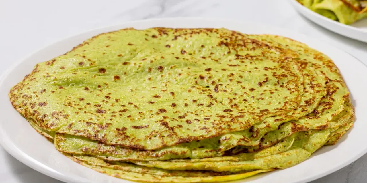 Piatto di crepes di zucchine verdi, sottili e leggermente dorate, impilate su un piatto bianco.