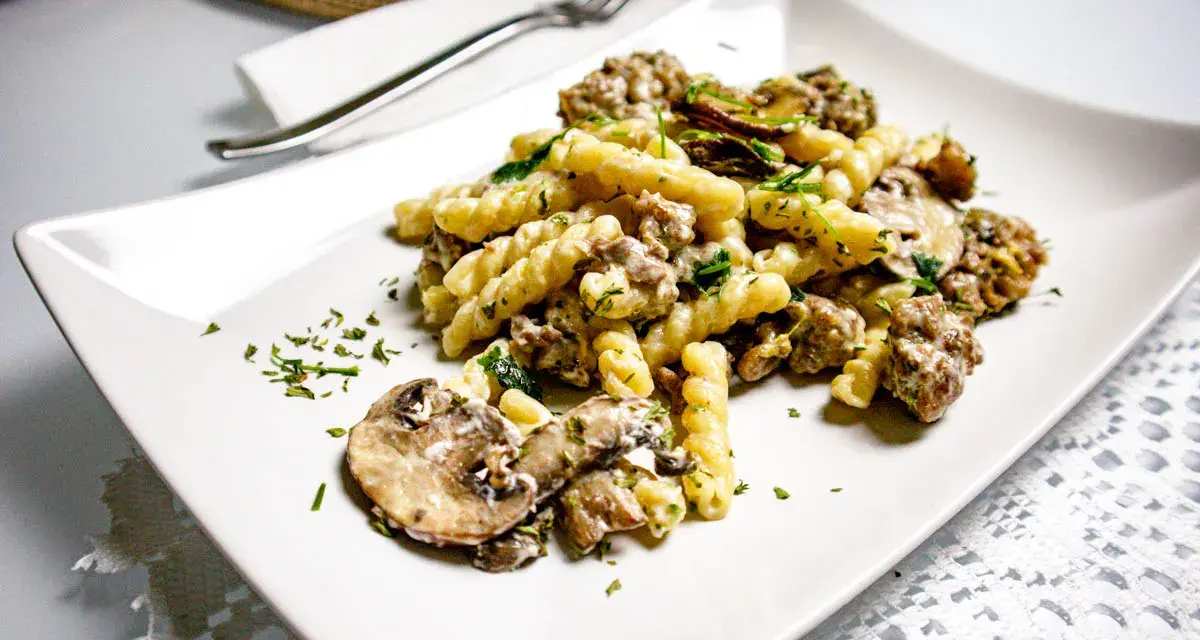 Un piatto di pasta salsiccia e funghi, condito con prezzemolo fresco, servito su un piatto bianco.