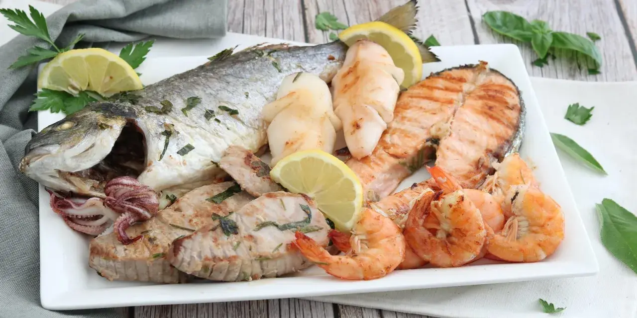 Un piatto invitante di grigliata di pesce: orata intera, tranci di salmone, gamberi, calamari e tonno, guarnito con limone e prezzemolo.