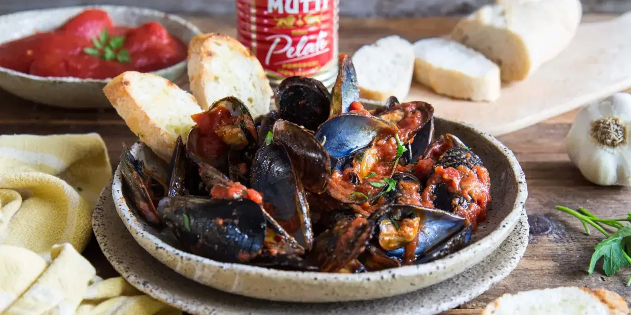 Piatto fumante di cozze alla tarantina ricetta, con pane tostato e pomodori pelati Mutti.