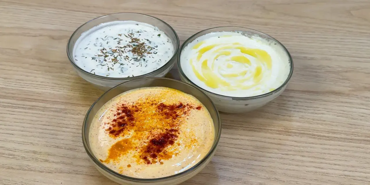 Tre ciotole di salsa con yogurt greco: una con erbe, una con olio d'oliva e una con paprika.