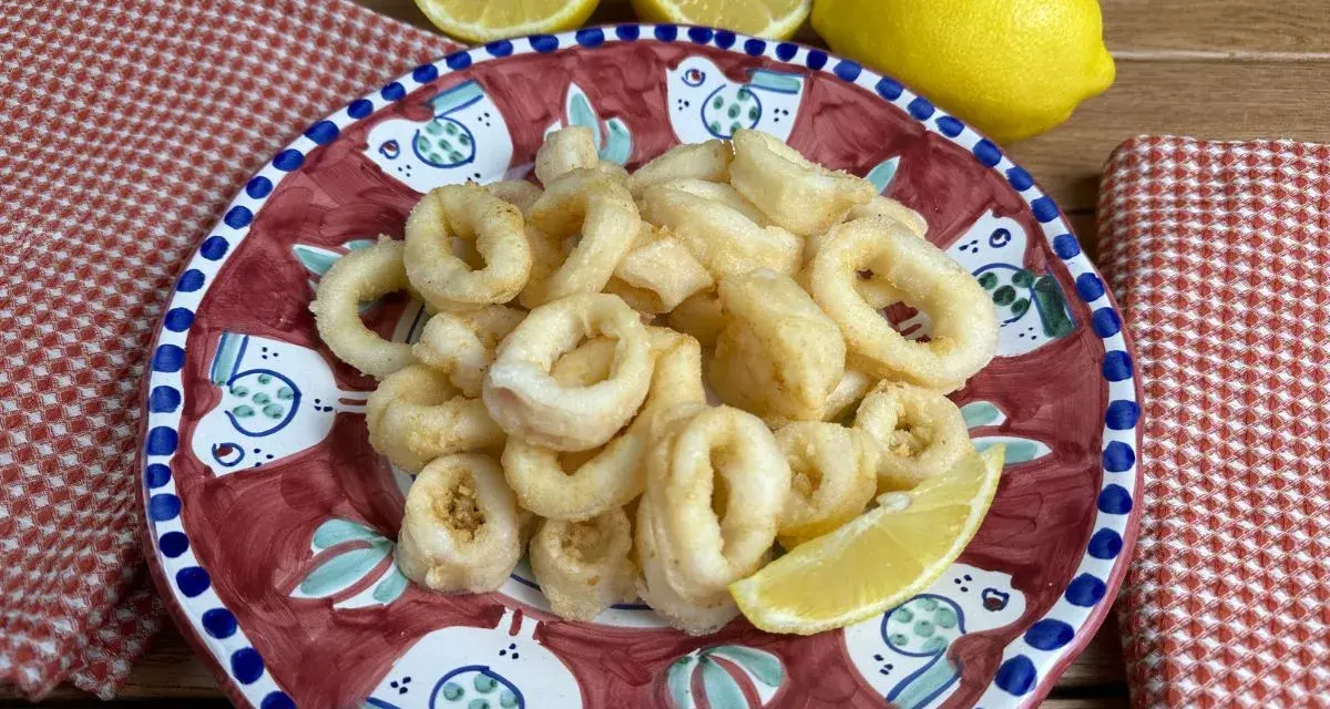 Un piatto di **calamari fritti** dorati, guarnito con spicchi di limone fresco, su un piatto decorato con uccelli stilizzati.