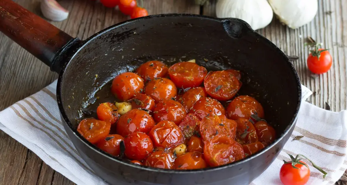 Pomodorini confit in padella, dolci e succosi, cotti con aglio e erbe aromatiche. Un contorno saporito e profumato.