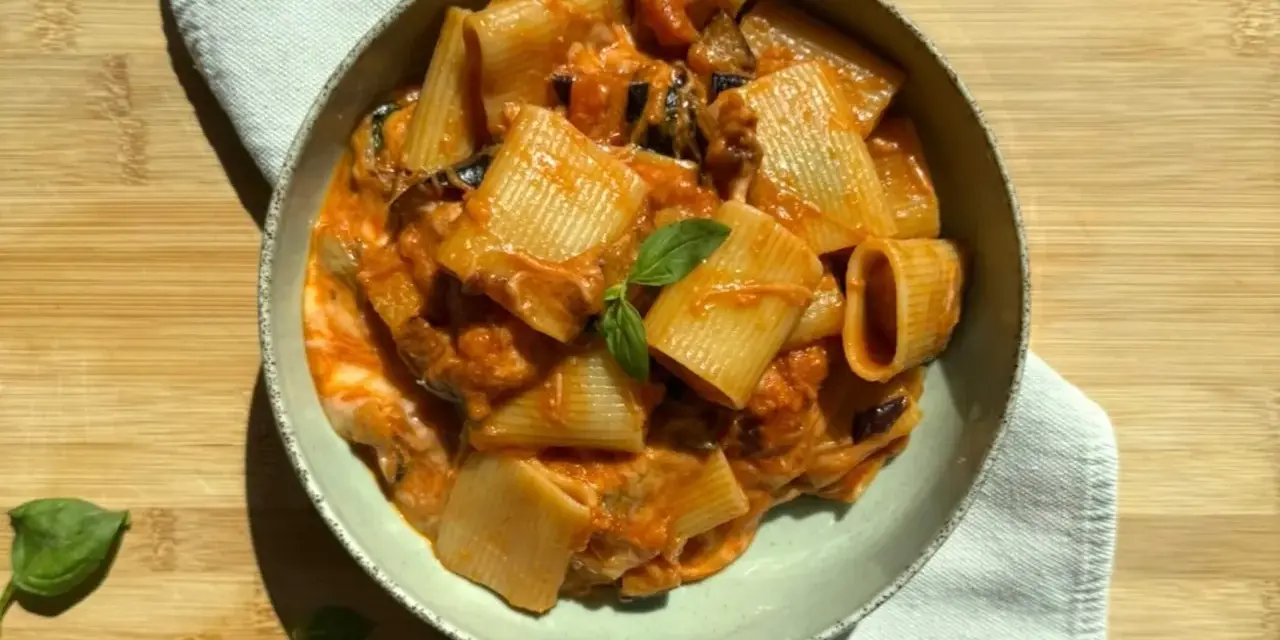 Un piatto di pasta alla siciliana con rigatoni, melanzane e una salsa cremosa al pomodoro, guarnito con basilico fresco.