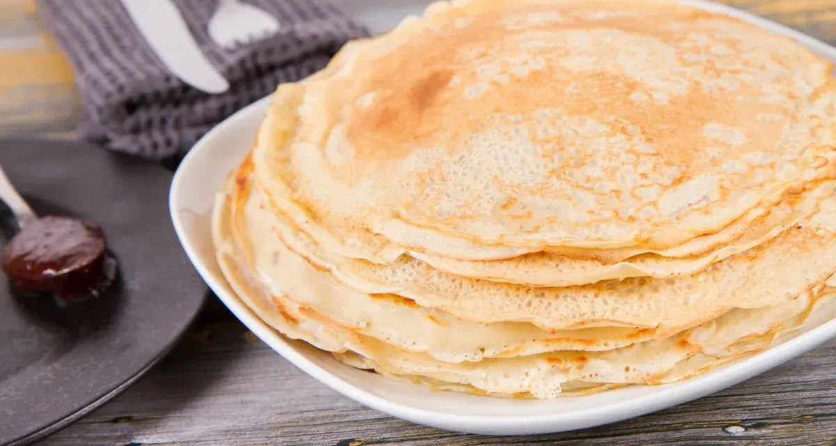 Pila di crepes senza uova, dorate e soffici, pronte per essere farcite. Accanto, un cucchiaino di marmellata.