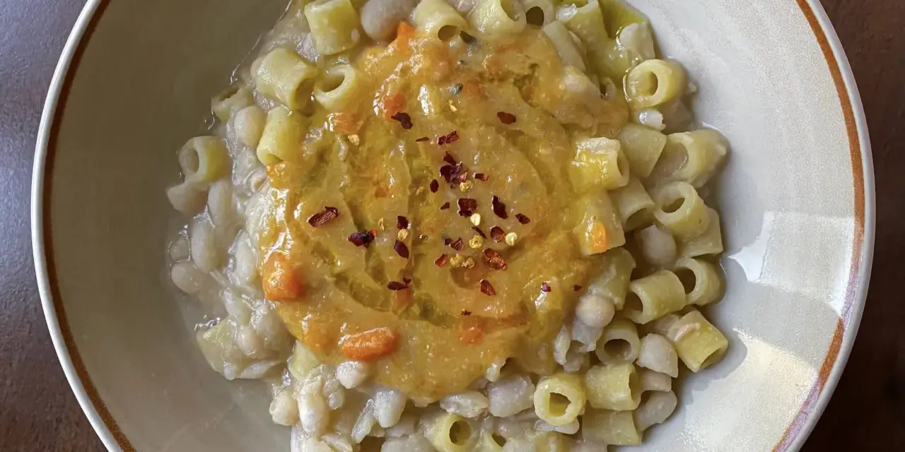Un piatto di pasta e fagioli estiva, con ditalini e fagioli cannellini, guarnito con una purea di verdure e peperoncino.