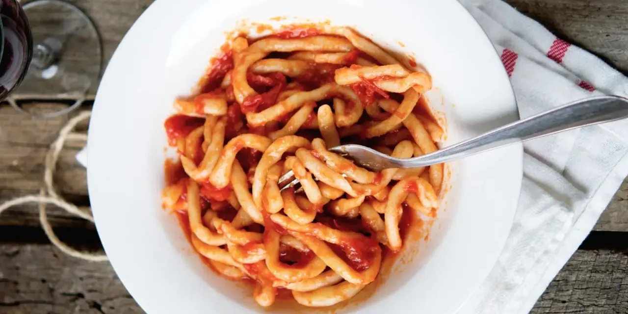 Piatto di pasta fresca condita con un saporito sugo all'aglione, servito su un piatto bianco con una forchetta.