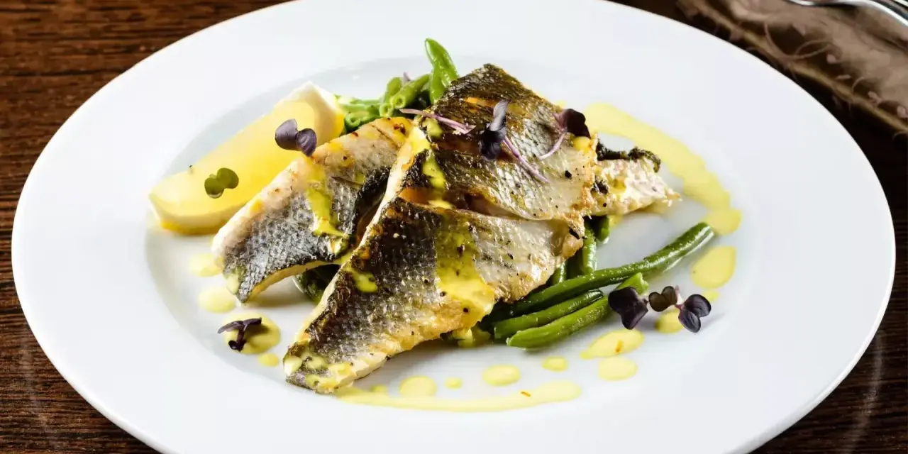 Deliziosi secondi di pesce con fagiolini croccanti, limone e una salsa gialla cremosa, guarniti con erbe viola.