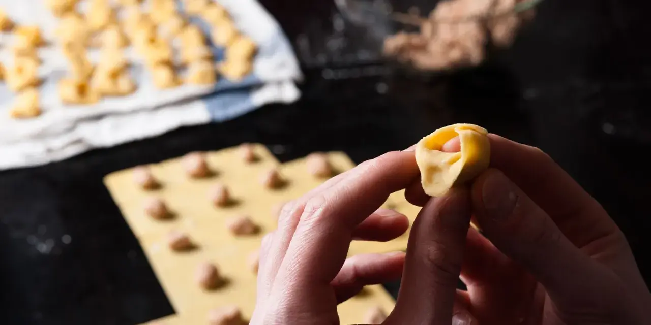 Mani che creano tortellini fatti in casa, con la pasta fresca e il ripieno pronto.