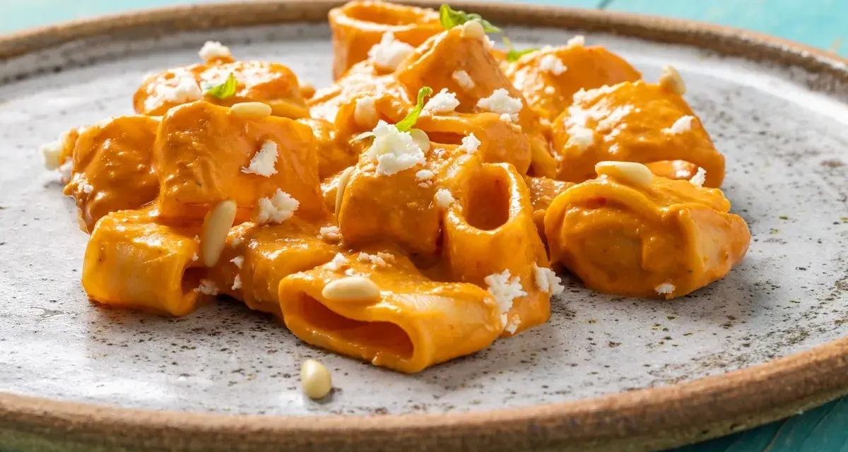 Paccheri cremosi con salsa arancione, formaggio sbriciolato e pinoli. Un piatto che ricorda il sapore del brodo vegetale Bimby.