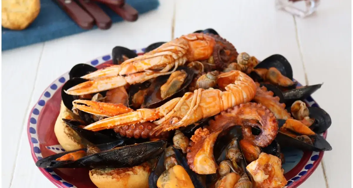 Un piatto ricco di zuppa di cozze, scampi e polpo, servito con pane tostato.