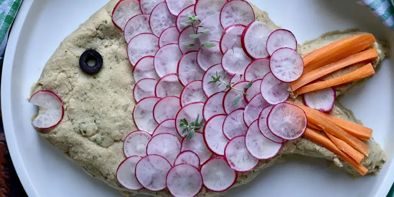 Pesce finto ricetta: un impasto cremoso decorato con ravanelli affettati, carote a bastoncino, un'oliva e erbe aromatiche.