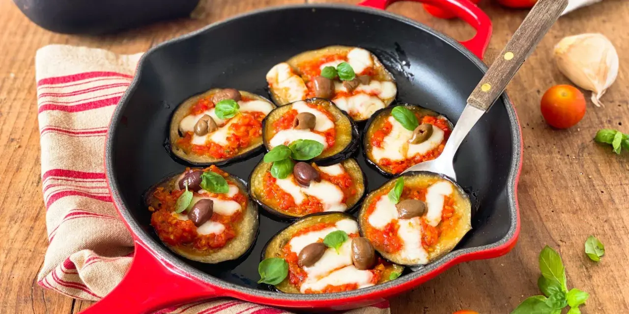 Melanzane in padella con pomodoro e mozzarella, guarnite con olive e basilico. Un antipasto invitante e saporito.
