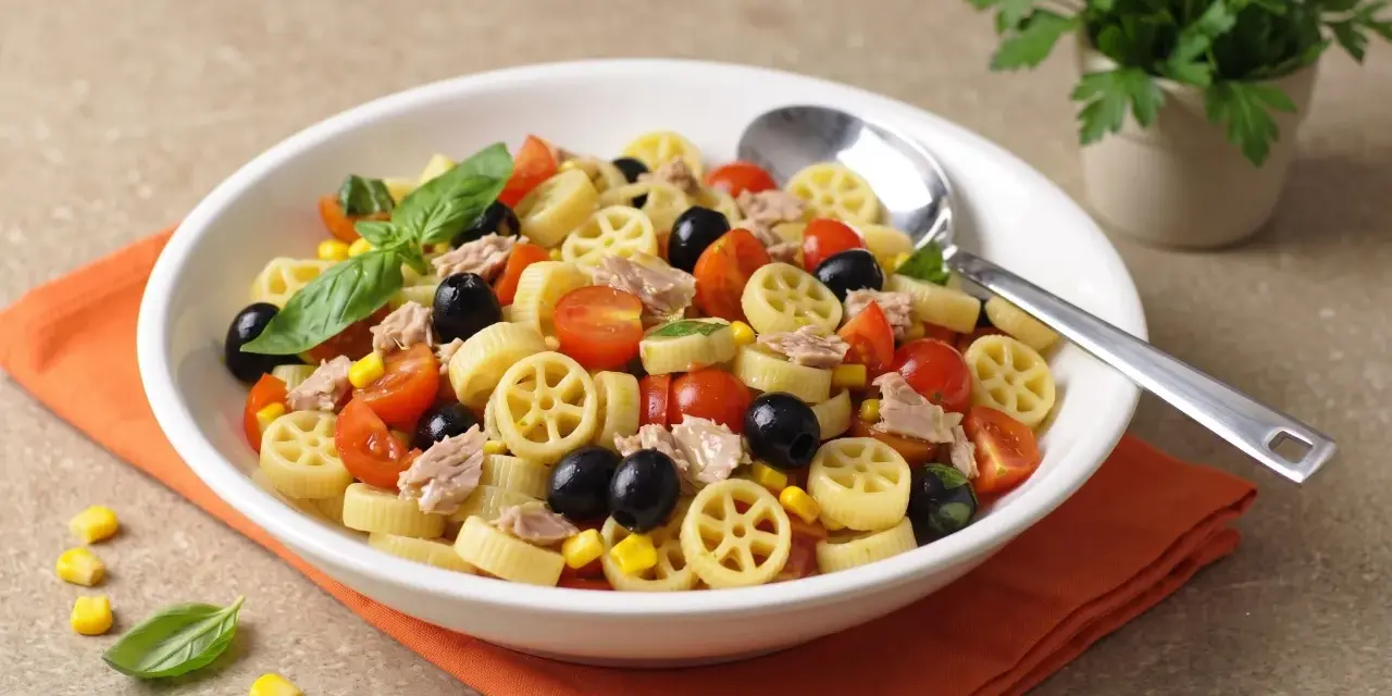 Un piatto invitante di pasta fredda tonno con pomodorini, olive nere, mais e basilico fresco. Perfetta per un pranzo estivo.