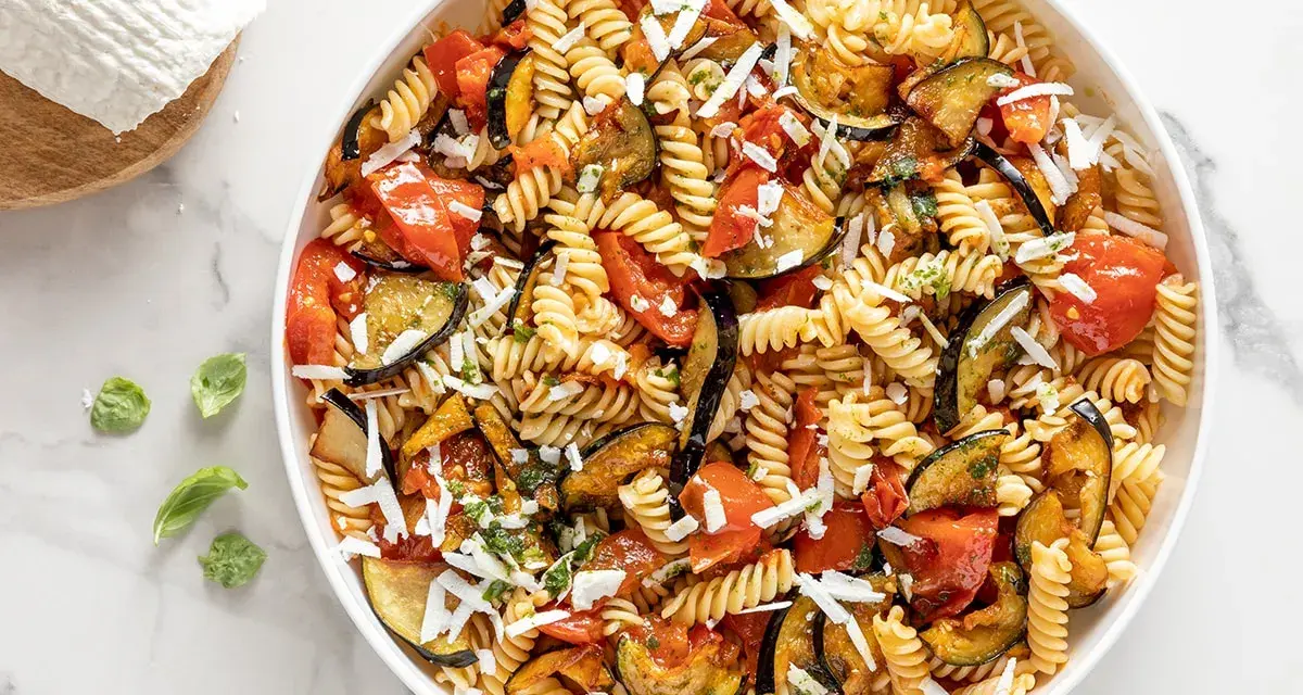 Un piatto invitante di pasta fredda alla norma con melanzane, pomodori e ricotta salata grattugiata.