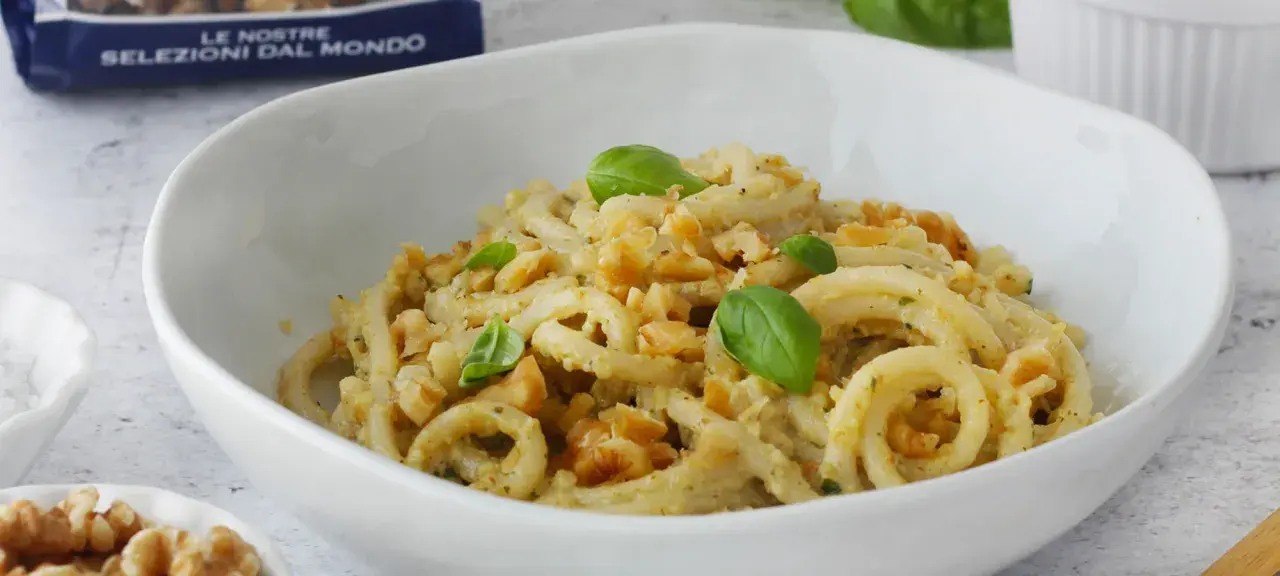 Pasta condita con un cremoso pesto di noci, guarnita con basilico fresco e noci croccanti.