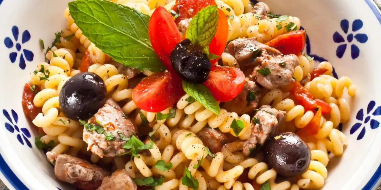 Fusilli con pesce spada, pomodorini, olive nere e menta fresca in una ciotola decorata.
