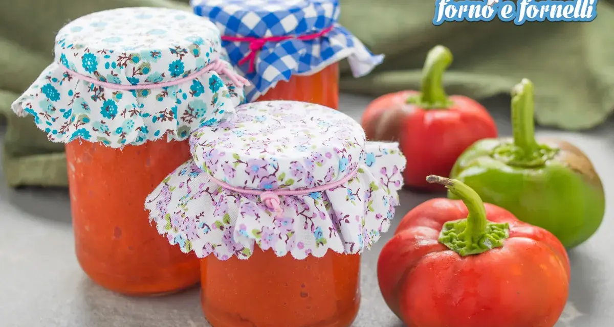 Barattoli di salsa di peperoni fatti in casa, decorati con stoffe floreali e a quadretti, accanto a peperoni freschi.