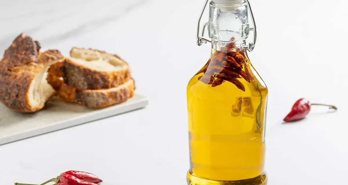 Olio al peperoncino in bottiglia, con pane rustico e peperoncini rossi. Un tocco piccante per ogni piatto.