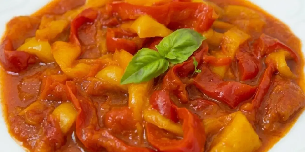 Un piatto di peperonata ricetta, con peperoni rossi e gialli cotti in salsa, guarnito con basilico fresco.