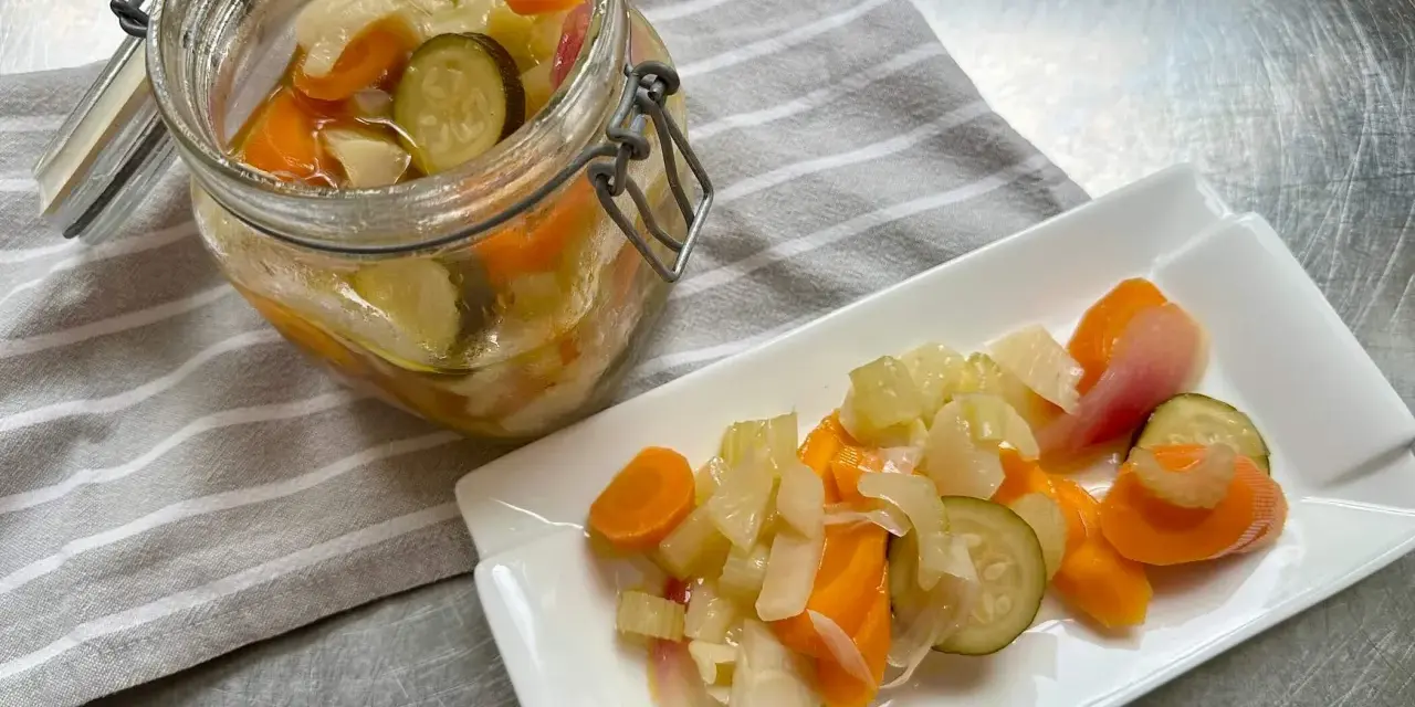 Giardiniera fatta in casa: carote, sedano, cipolle e cetrioli sottaceto in un barattolo e su un piatto. Ricetta facile e gustosa.