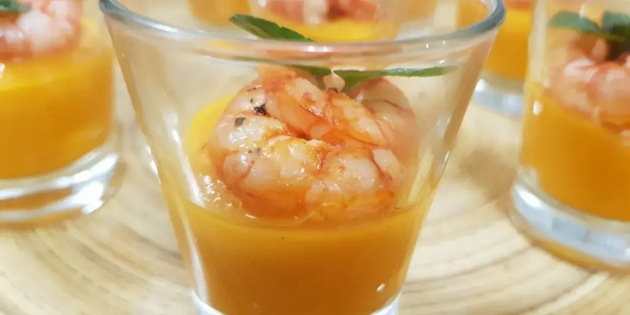 Deliziosi finger food gamberi su crema arancione in bicchierini, guarniti con menta.