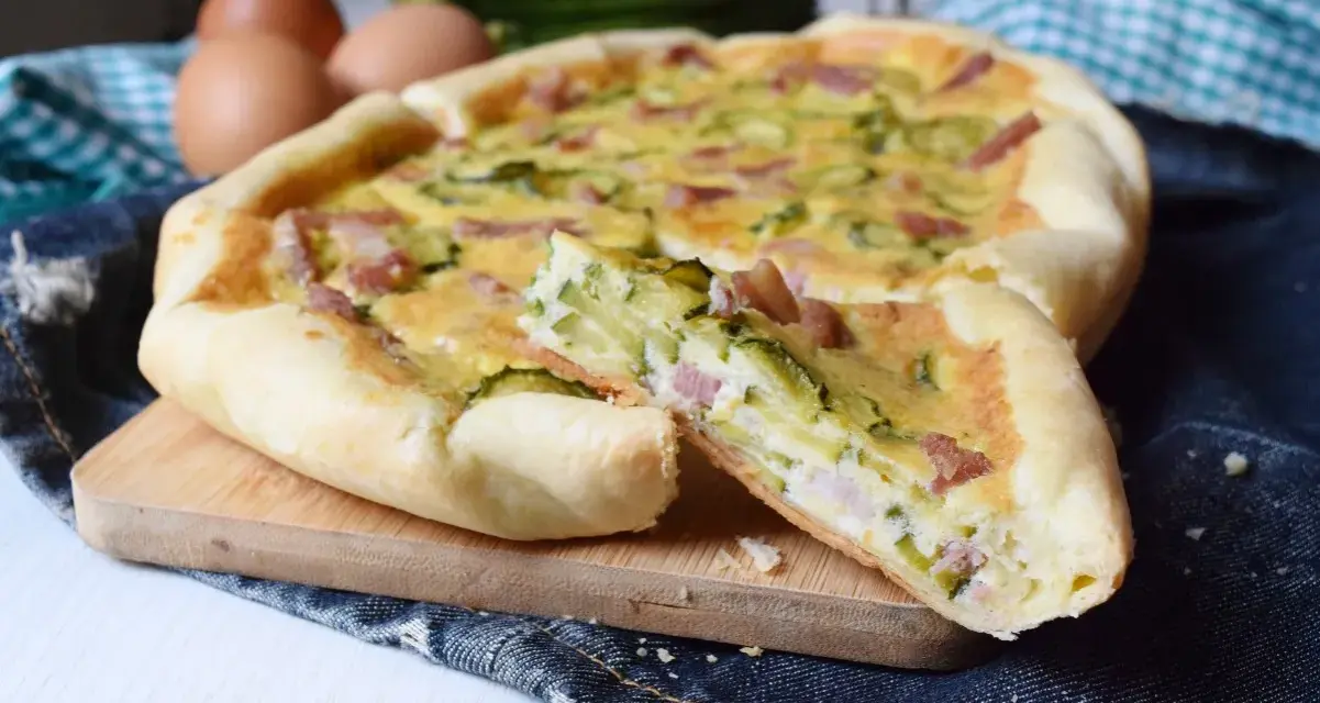 Torta salata con zucchine e pancetta, una fetta tagliata mostra il ripieno gustoso. Ingredienti freschi e profumati.