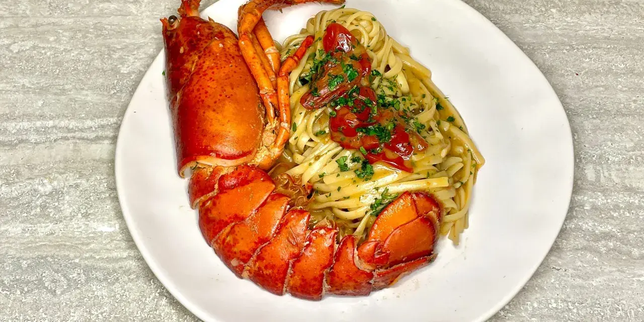 Un piatto di linguine all'astice, con pasta condita e astice intero, guarnito con pomodorini e prezzemolo.