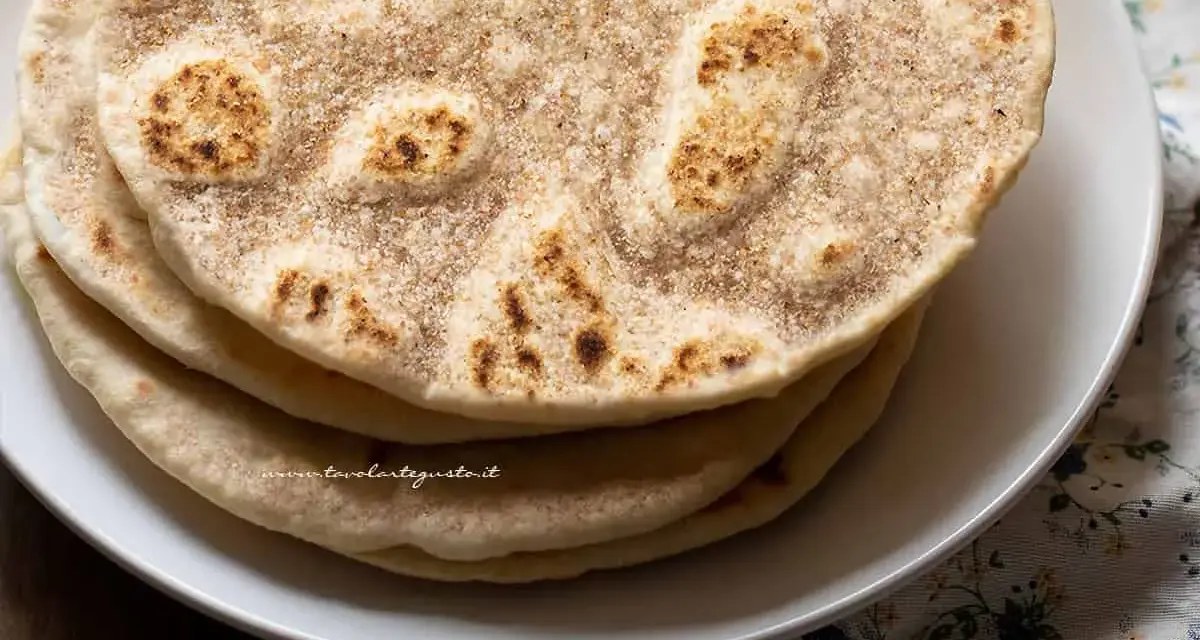 Piatto di piadine senza strutto, dorate e leggermente maculate, impilate su un piatto bianco.