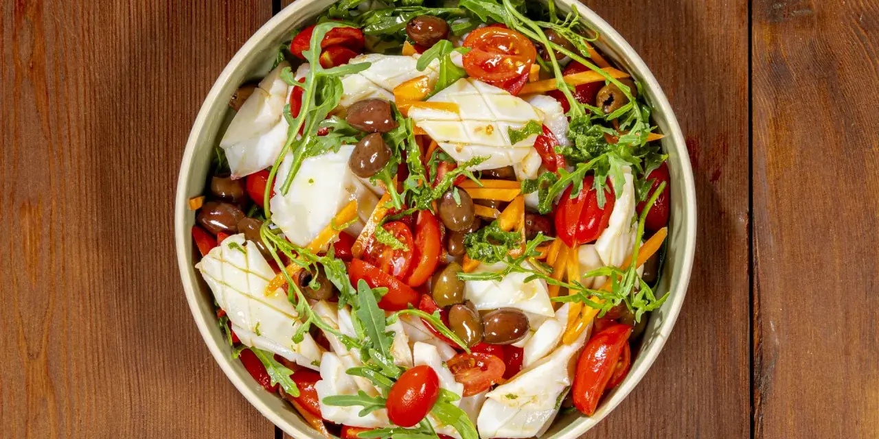 Insalata di calamari fresca con pomodorini, olive, rucola e carote julienne, un piatto leggero e saporito.