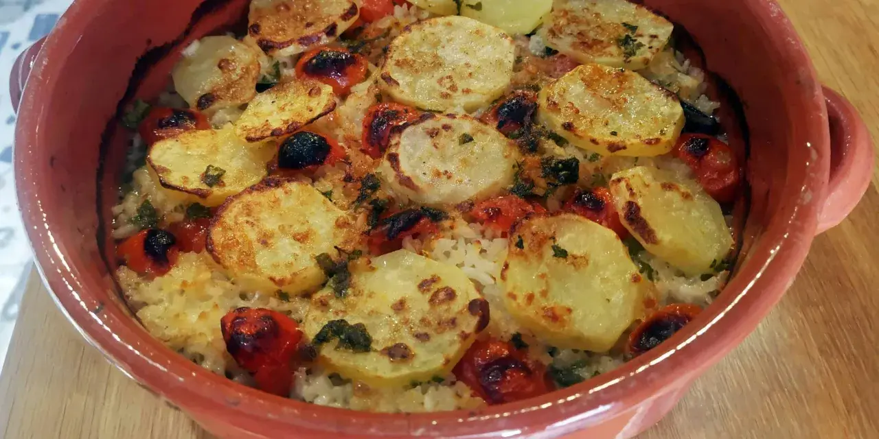 Piatto di riso patate e cozze cotto al forno, con pomodorini e erbe aromatiche, servito in una terrina di terracotta.