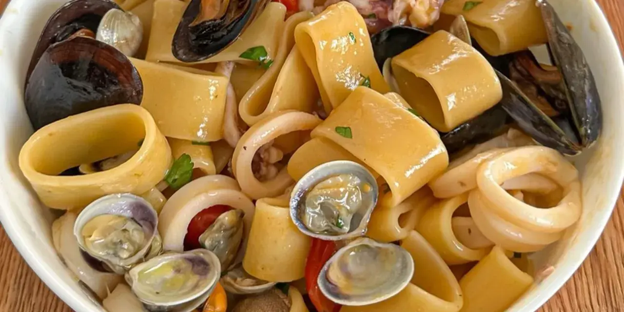 Calamarata allo scoglio ricca di cozze, vongole e anelli di calamaro, un piatto di mare invitante.