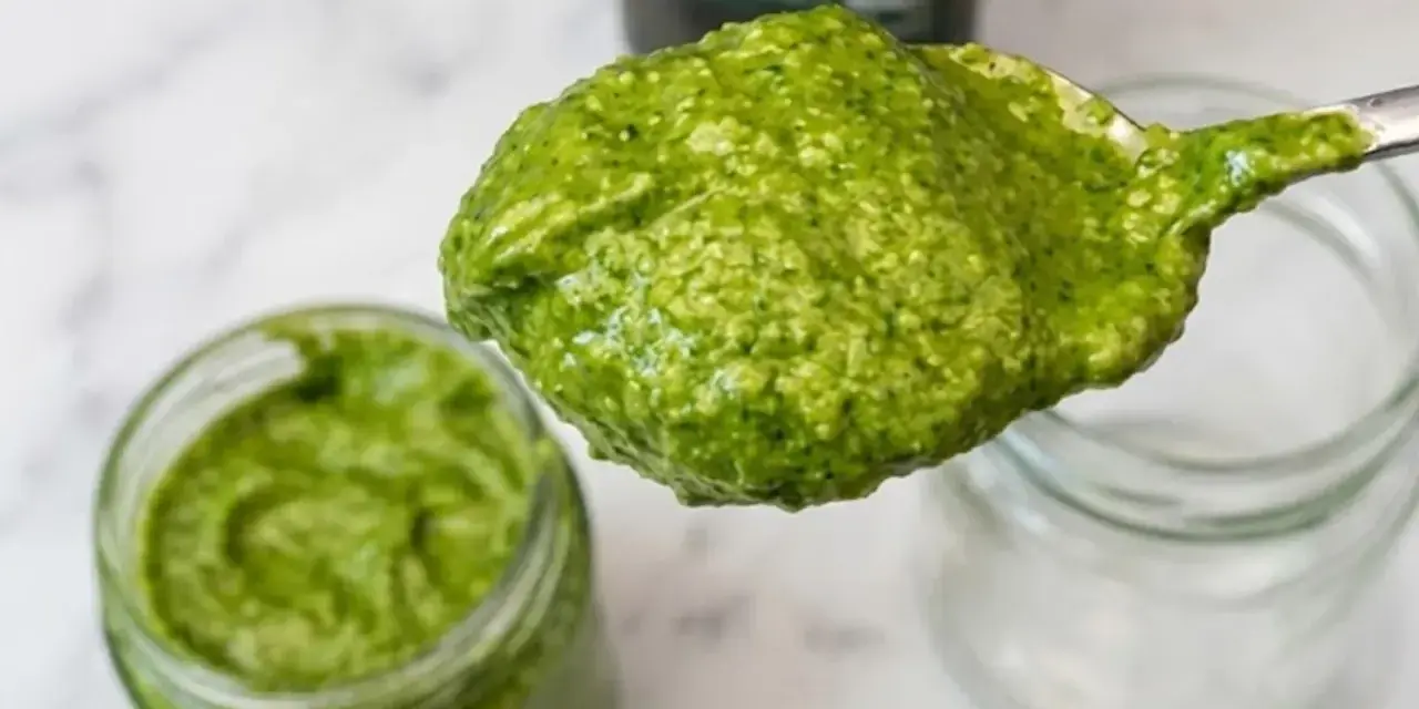 Cucchiaio pieno di pesto senza pinoli, cremoso e verde brillante, accanto a un barattolo.