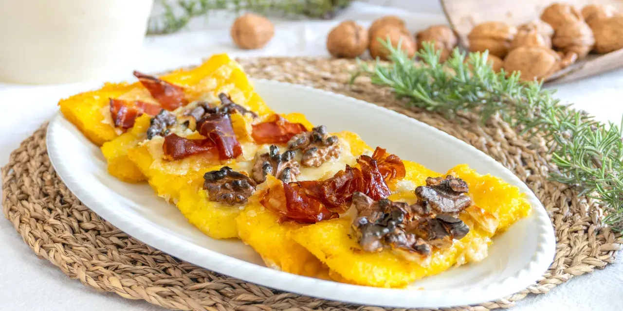 Deliziosi crostini di polenta freddi con prosciutto croccante e noci, un antipasto rustico e saporito.