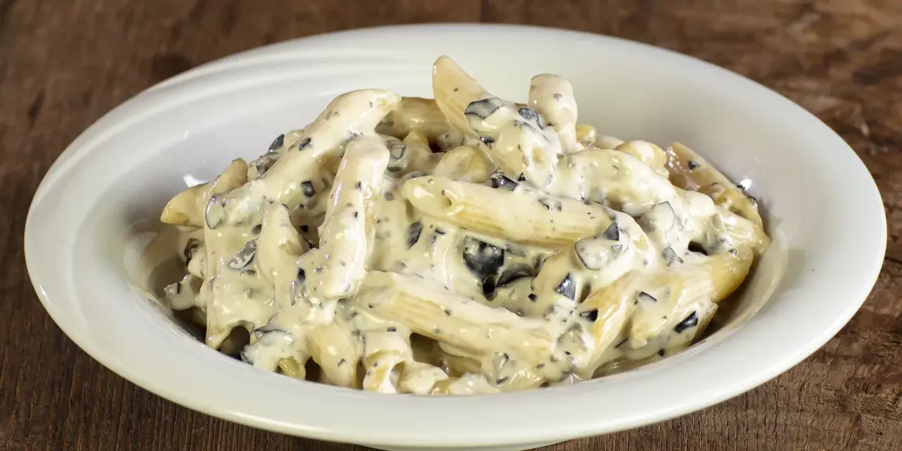 Penne cremose con pezzetti scuri, un piatto invitante di pasta alla cenere, servito in una ciotola bianca su un tavolo di legno rustico.