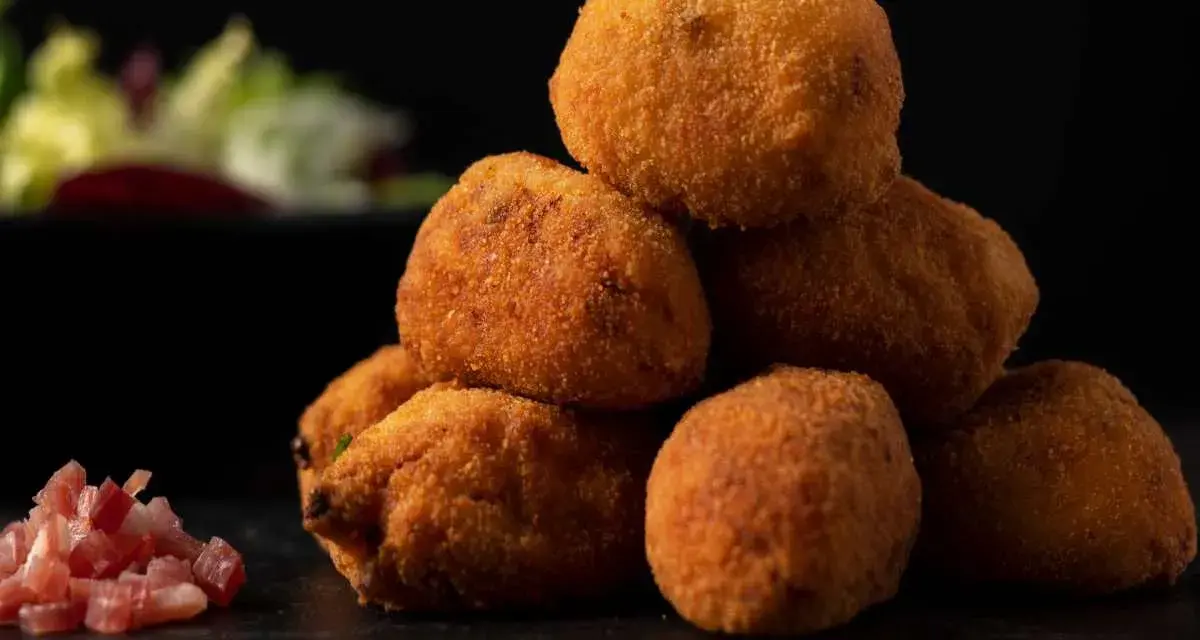 Pile di supplì alla carbonara dorati e croccanti, con guanciale a cubetti e insalata sfocata sullo sfondo.