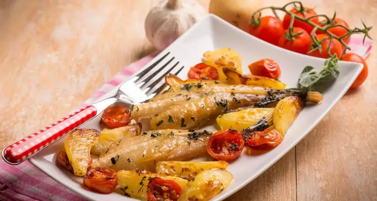 Piatto di coda di rospo al forno con patate arrosto e pomodorini. Un contorno di erbe aromatiche completa il piatto.