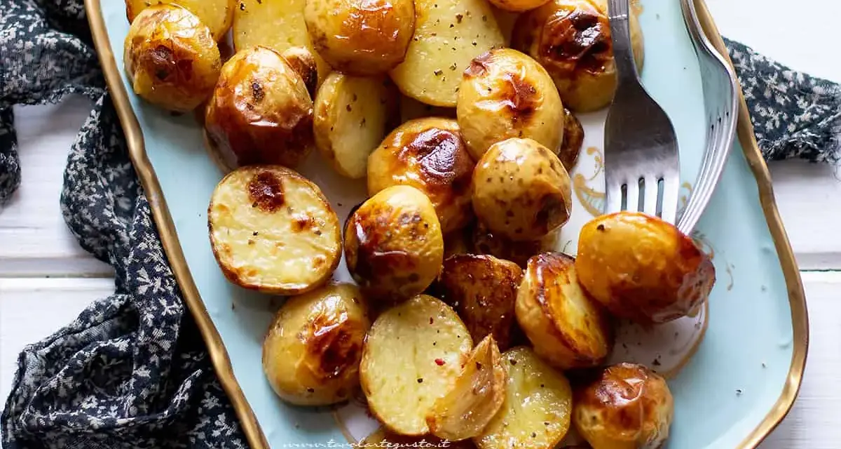 Patate novelle al forno dorate e croccanti, servite su un piatto azzurro con forchetta.