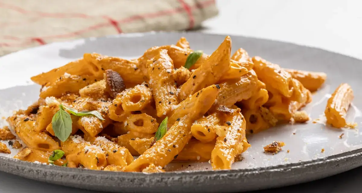Piatto di pasta con peperoni arrostiti, condita con una cremosa salsa arancione, parmigiano e basilico fresco.