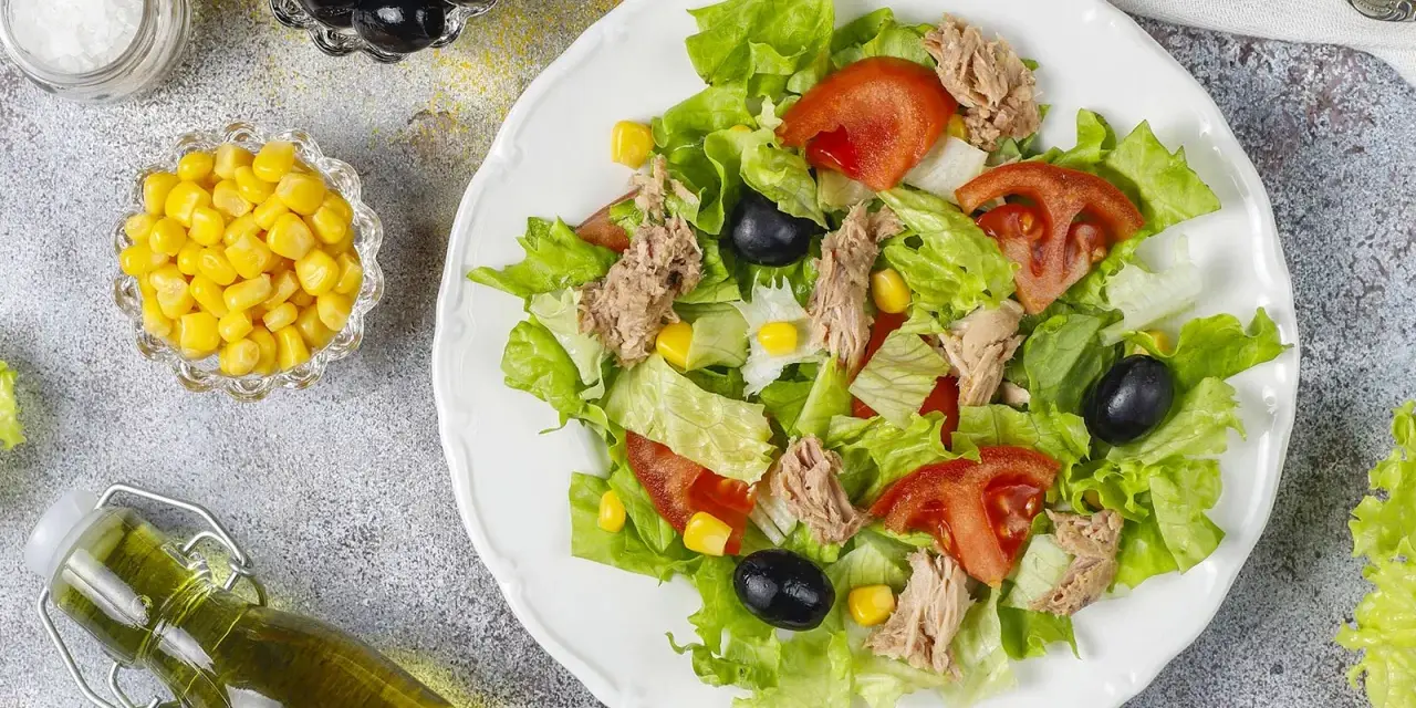 Deliziosa insalata di tonno con lattuga croccante, pomodoro, mais e olive nere. Un piatto fresco e leggero, perfetto per ogni occasione.