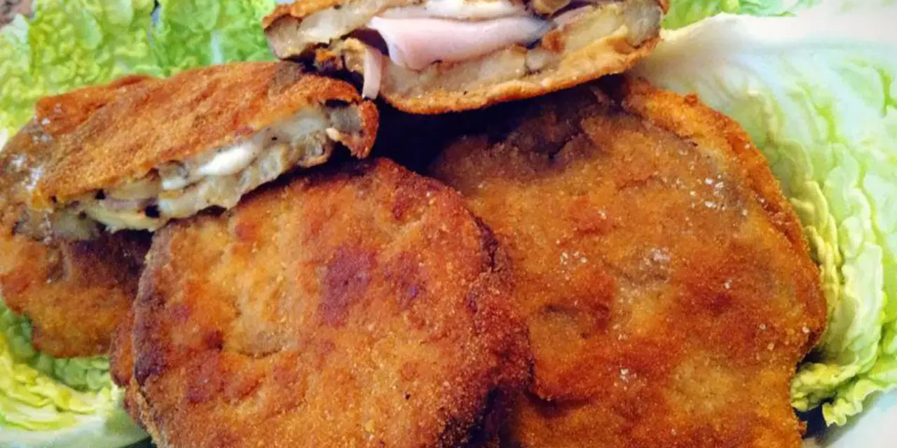 Cordon bleu di melanzane impanati e fritti, ripieni di prosciutto e formaggio filante, serviti su un letto di lattuga croccante.